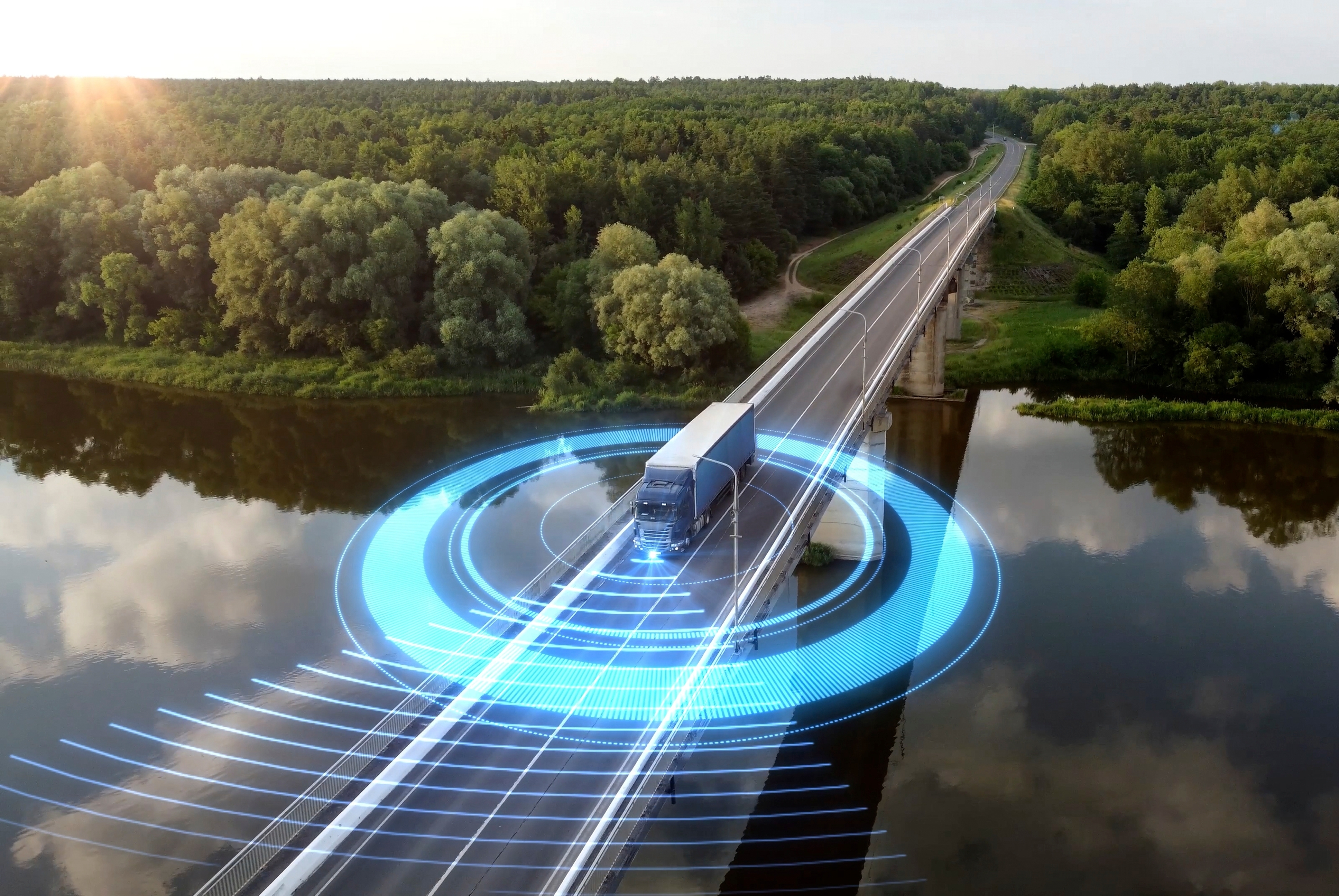 A semi-truck driving across a long bridge over a river, with a glowing blue digital overlay showing tracking rings and signals radiating from the vehicle.